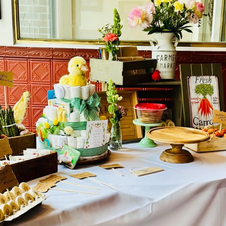 A table with farm-themed decorations, including a diaper cake, fresh produce, and baked goods.