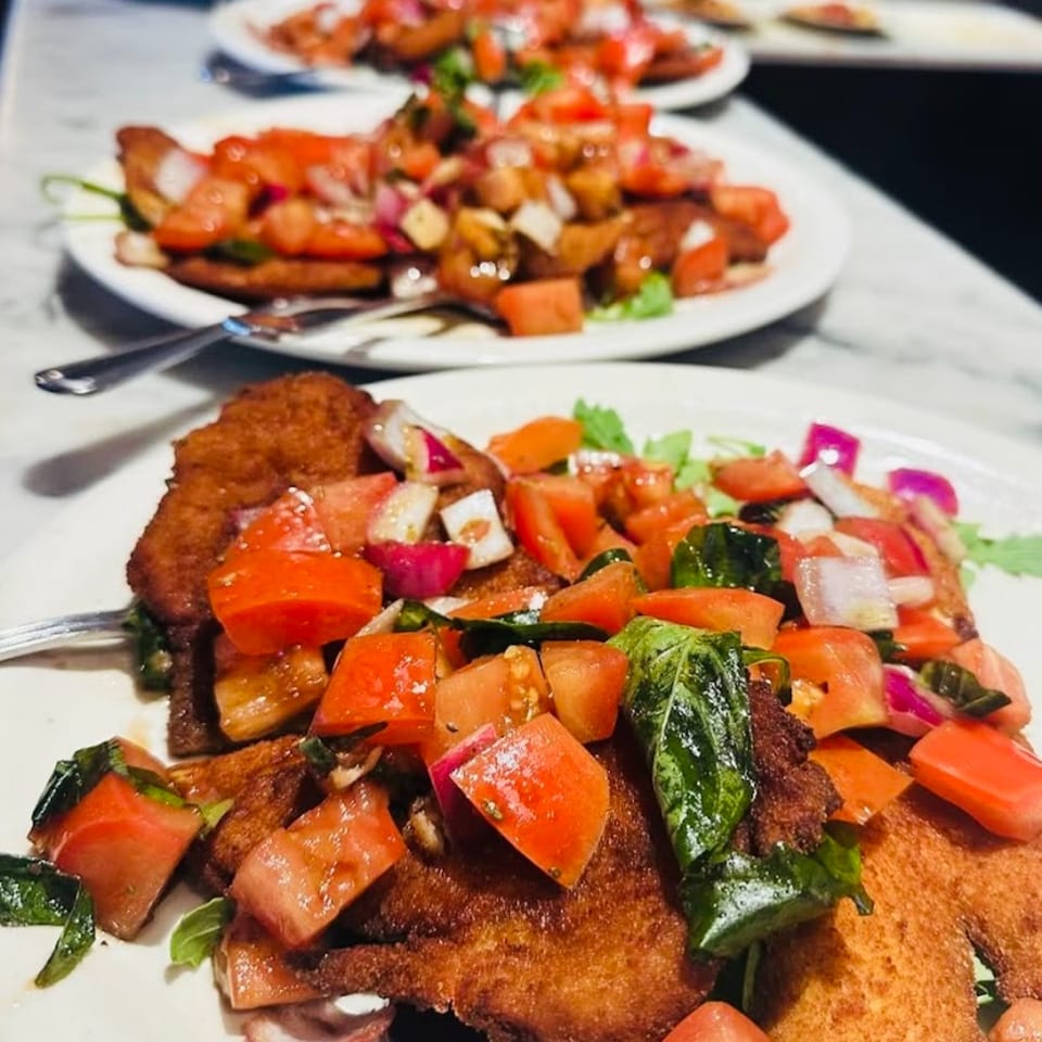 Two plates of Nick's Italian chicken cutlets topped with diced tomatoes, onions, and basil.