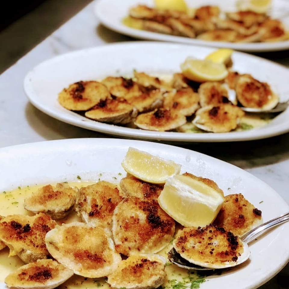 Two plates of baked clams with lemon wedges and butter sauce at Nick's Italian restaurant.