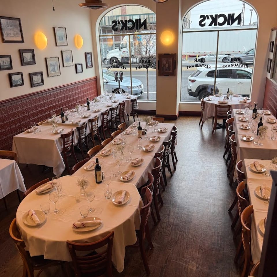 Interior of Nick's Italian restaurant with set tables, arched windows, and framed pictures on the wall.