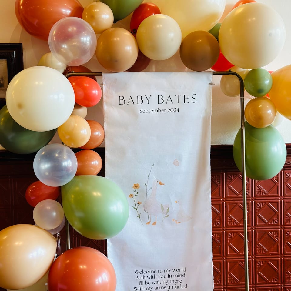 A white banner with "Baby Bates September 2024" and ducklings, surrounded by colorful balloons.