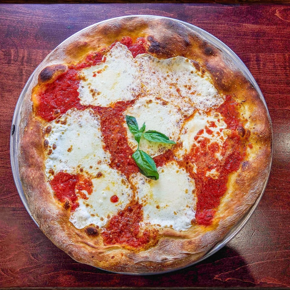 A freshly baked Nick's Italian pizza with melted mozzarella, red sauce, and basil on a wooden table.