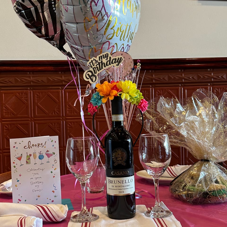Birthday celebration at Nick's with a bottle of Brunello wine, two wine glasses, and balloons.