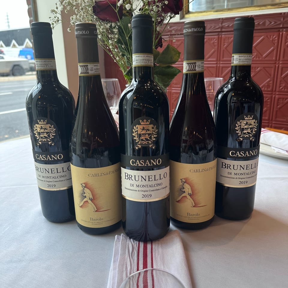 Five bottles of Italian red wine, including Brunello di Montalcino and Barolo, on a white tablecloth.