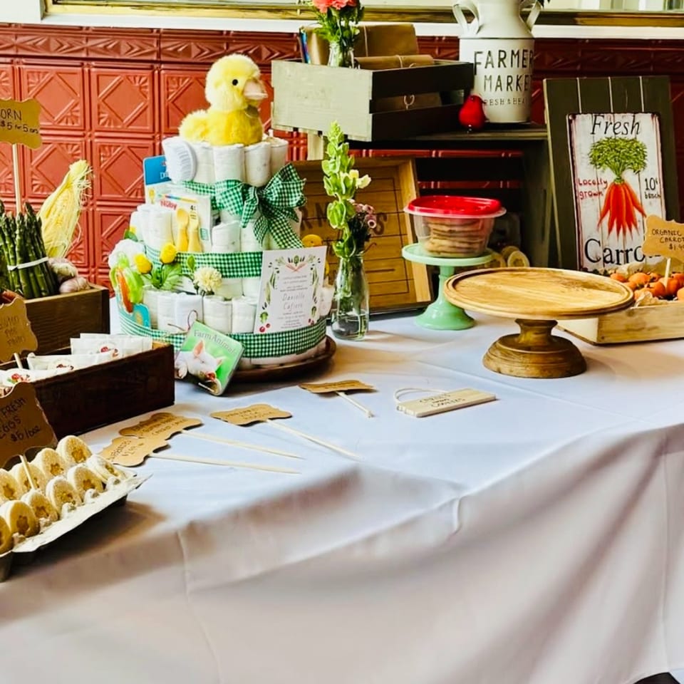A table with a diaper cake, fresh produce, and farm-themed decorations for a baby shower.