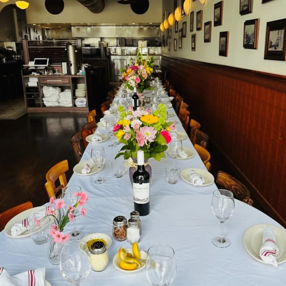 Long dining table set with white tablecloths, colorful floral centerpieces, wine bottles, and place settings.