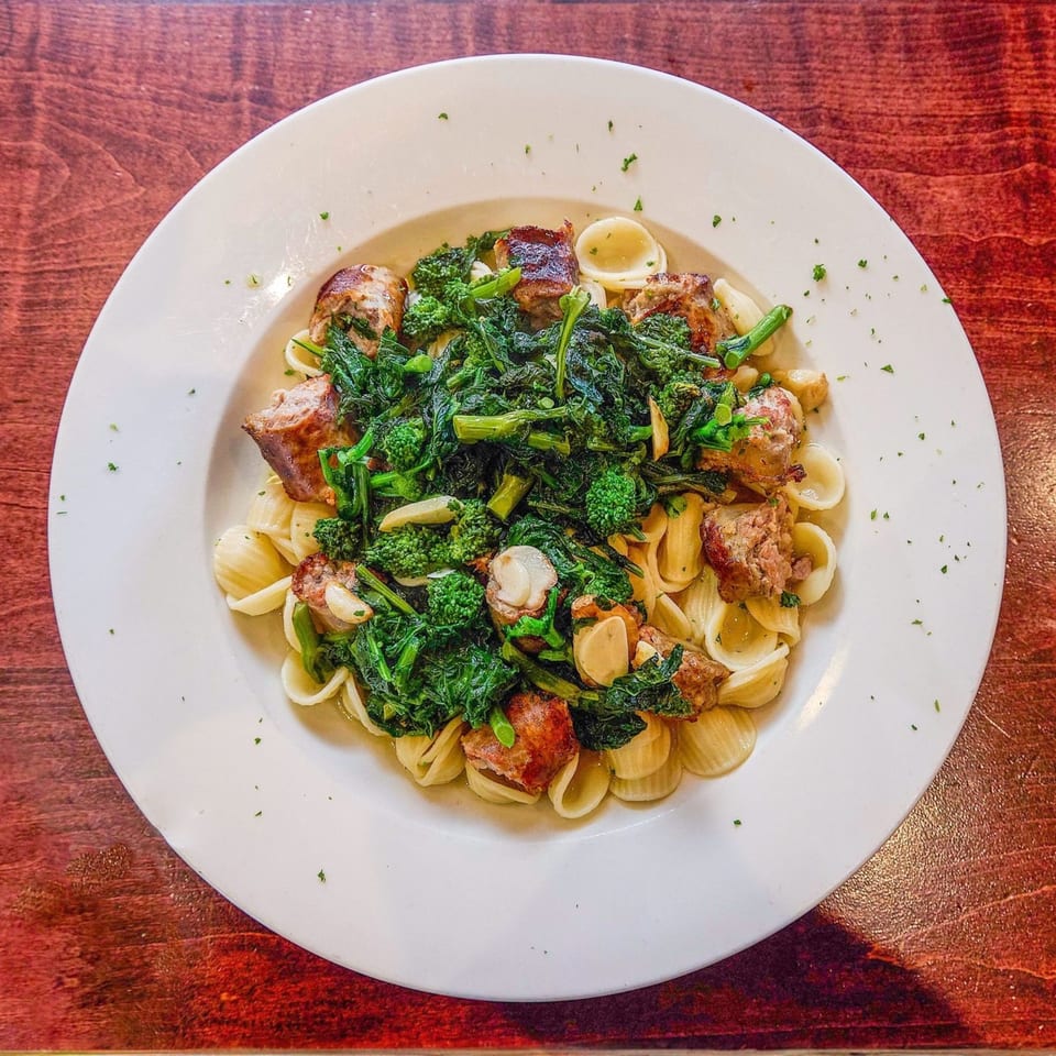 Orecchiette pasta with sausage, broccoli rabe, and garlic on a white plate at Nick's Italian restaurant.