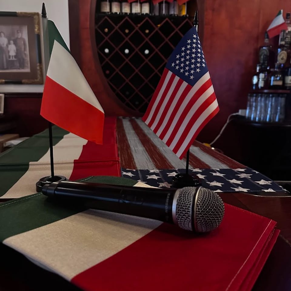 Italian and American flags with a microphone on a table runner, suggesting karaoke at Nick's.