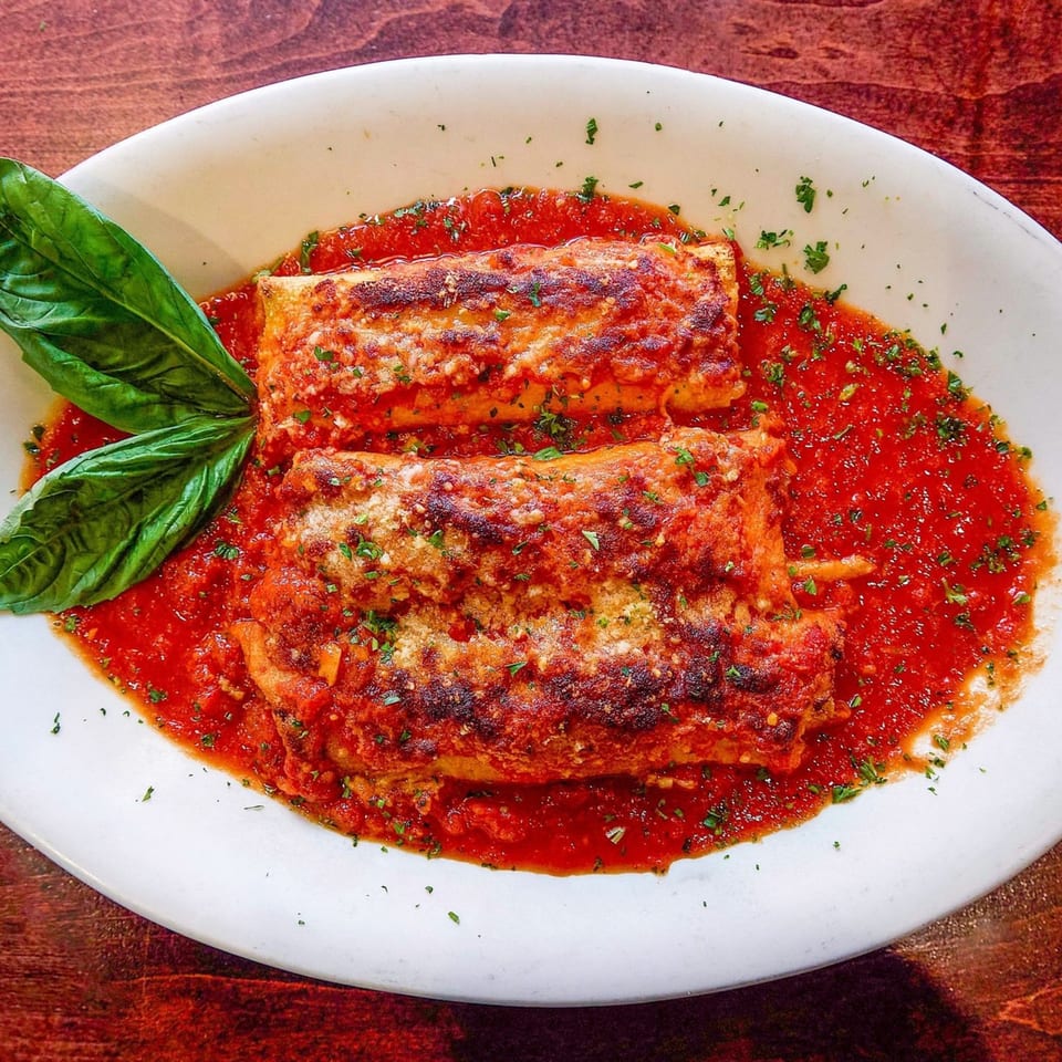 Two baked manicotti with rich red sauce, parmesan, and fresh basil on a white plate.