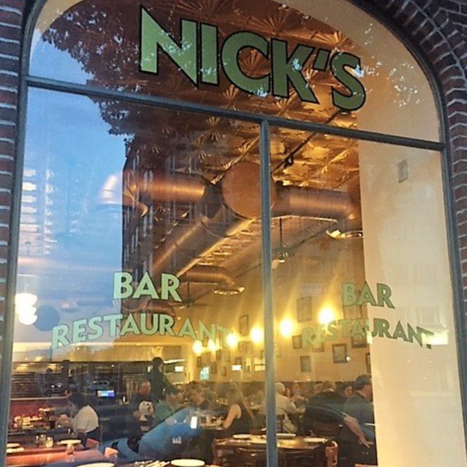 Exterior view of Nick's Italian restaurant through a large arched window, showing diners inside.