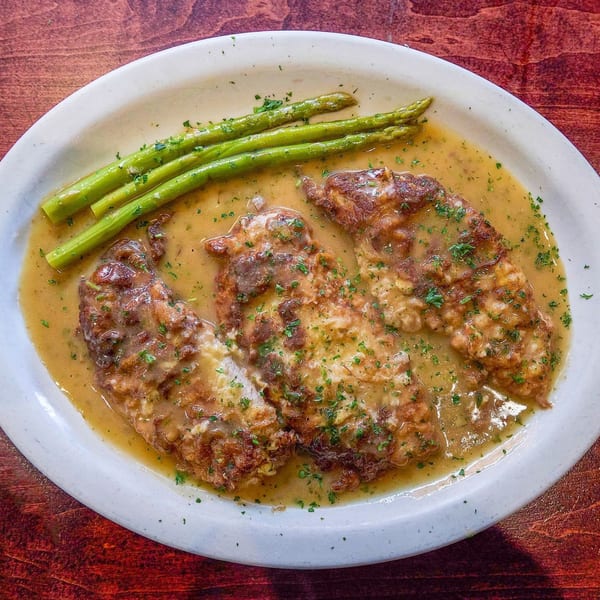 Three pieces of golden-brown chicken in a rich sauce, garnished with parsley and asparagus.