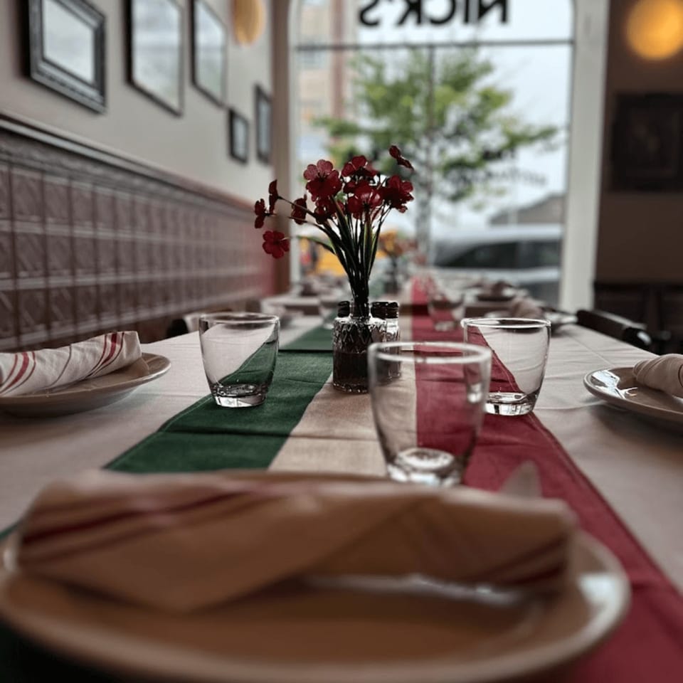 Set table at Nick's Italian restaurant with a red, white, and green runner and red flowers.