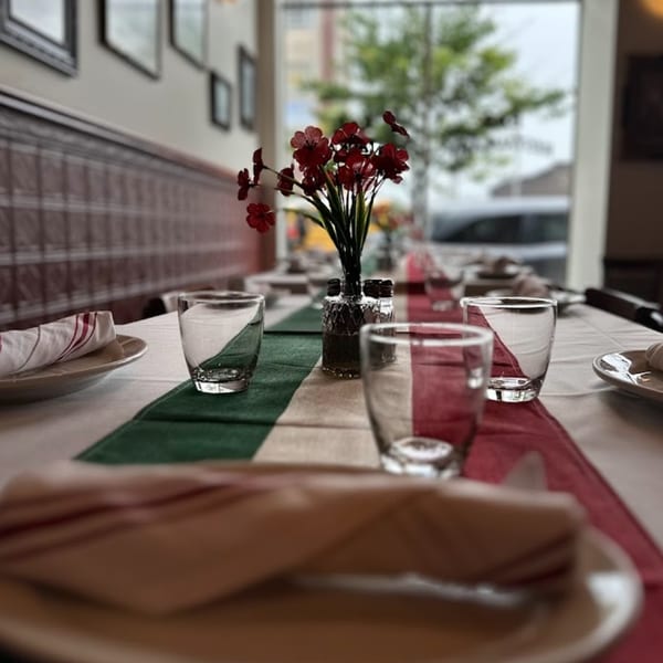 A set table at Nick's Italian restaurant with a red, white, and green runner and red flowers.