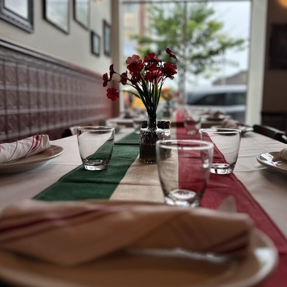 A set table at Nick's Italian restaurant with a red, white, and green runner and red flowers.