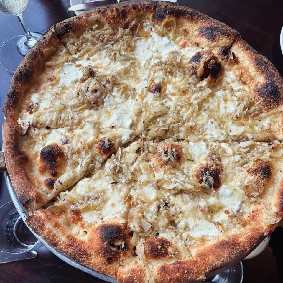 Overhead view of a Nick's Italian white pizza with caramelized onions and a charred crust.